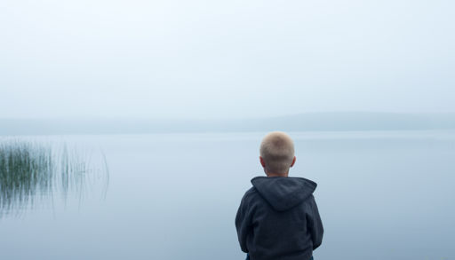 En mann som sitter på en stein og ser ut på vannet
