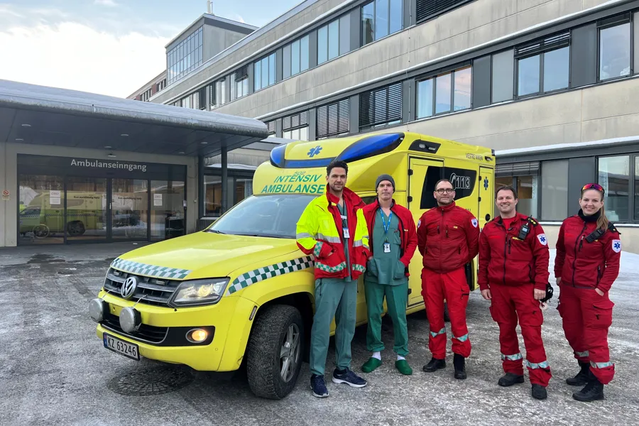 En gruppe mennesker i røde og gule dresser står ved siden av en gul bil