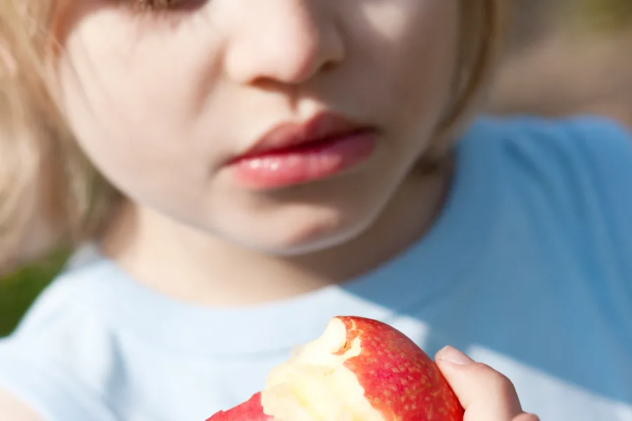 En barn holder et delvis oppspist eple i hånden ute i dagslys
