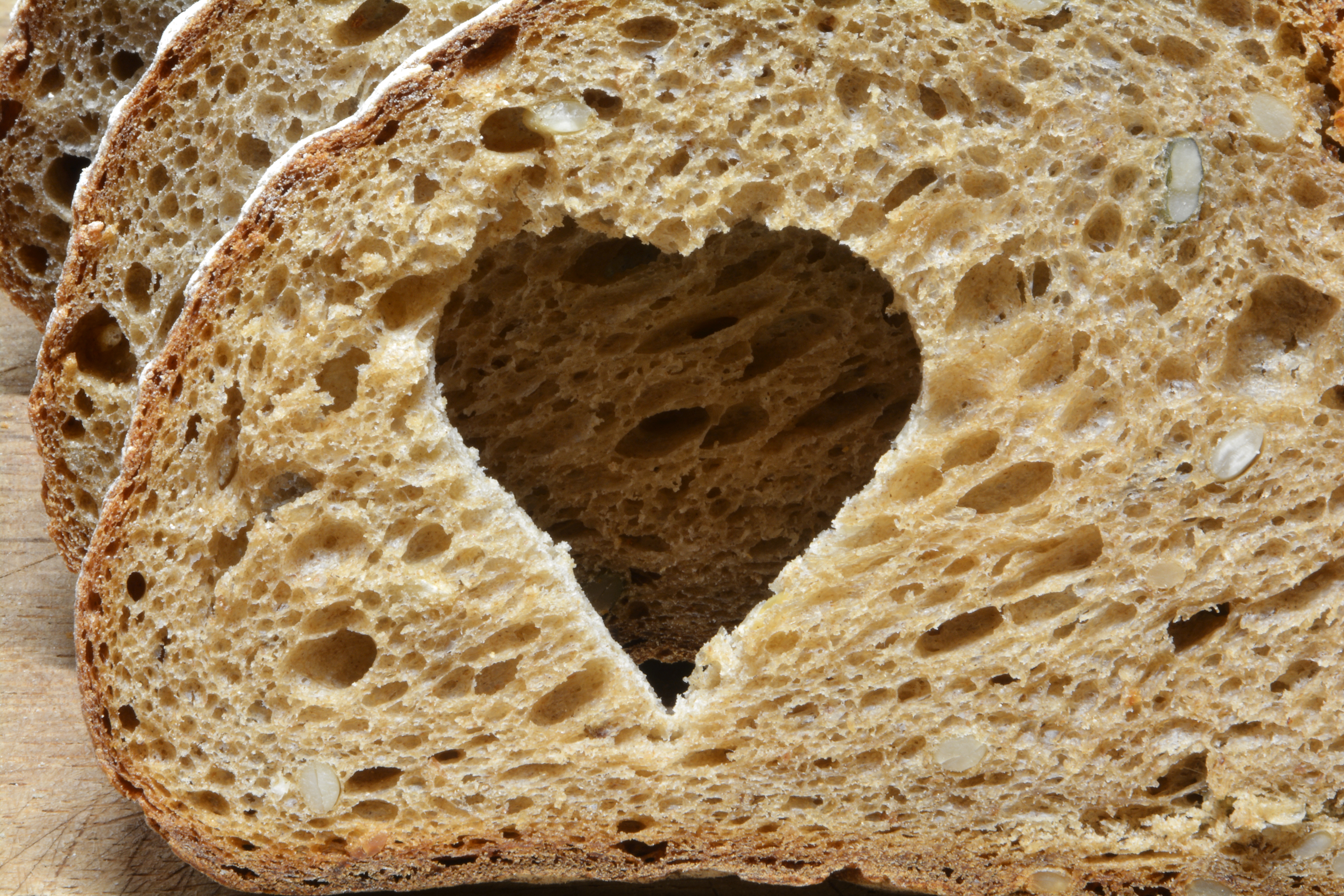 En skive grovbrød med et hjerteformet hull i midten vises i nærbilde.