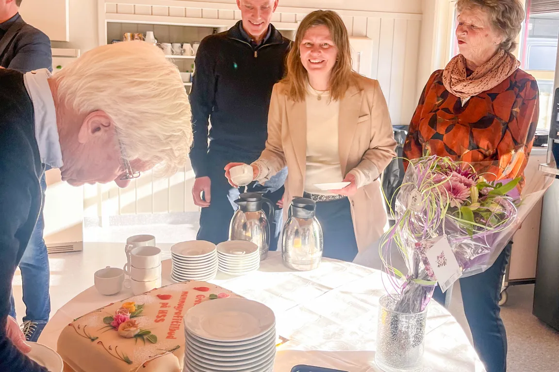 En gruppe mennesker som står rundt et bord med tallerkener og kopper