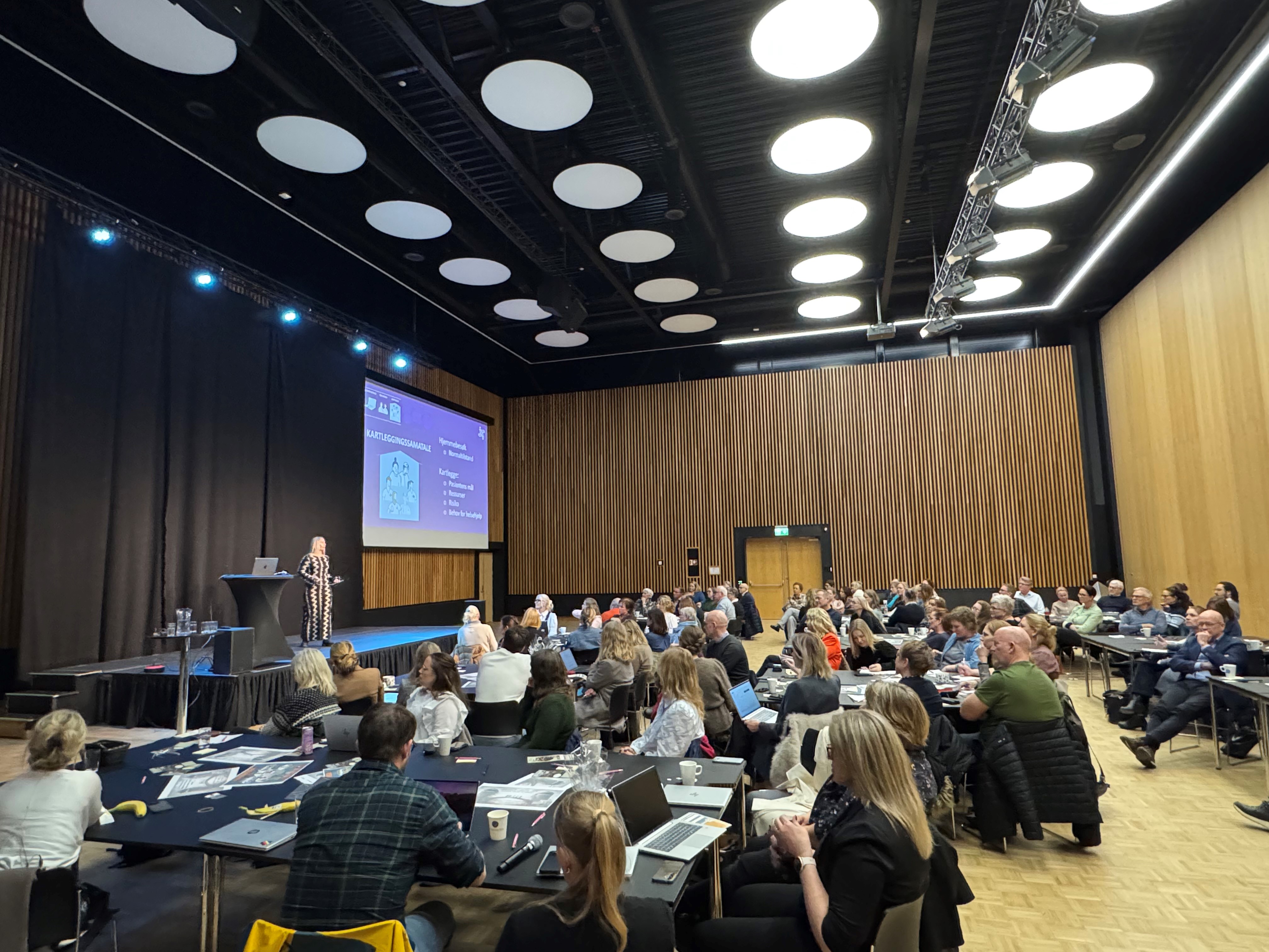 En gruppe mennesker som sitter i et rom med en stor skjerm