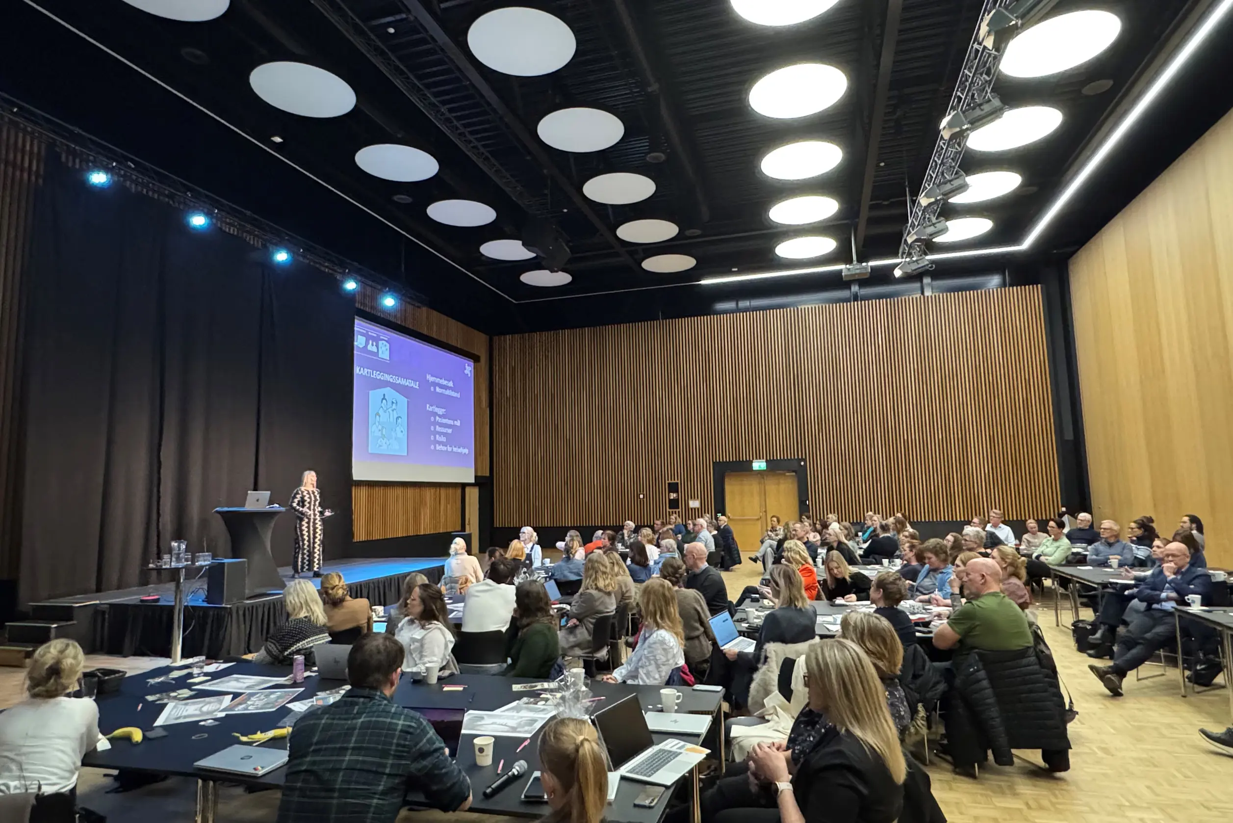 En gruppe mennesker som sitter i et rom med en stor skjerm