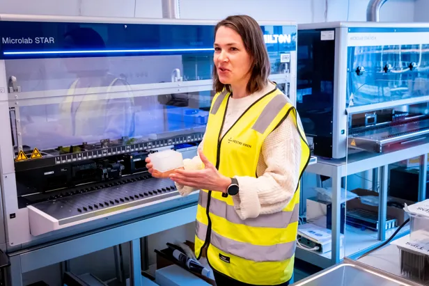 En mann i en gul jakke som holder en hvit gjenstand foran en maskin