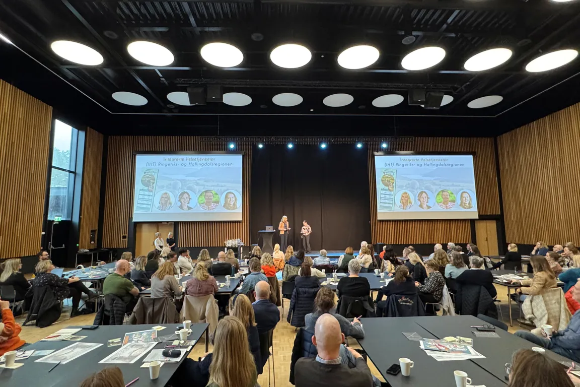 En gruppe mennesker som sitter i et rom med en stor skjerm