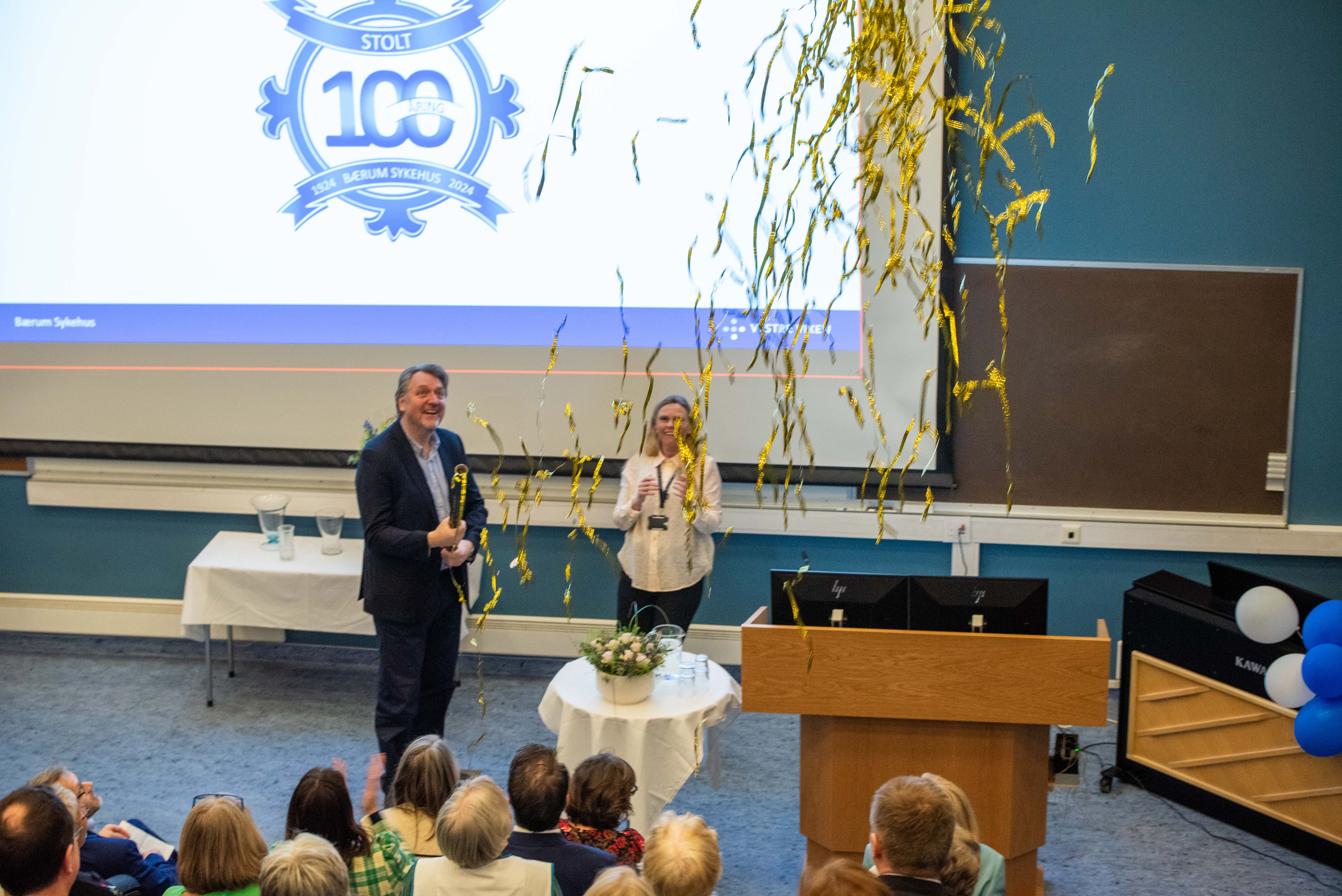 En mann og kvinne som står på en scene med en folkemengde som ser på