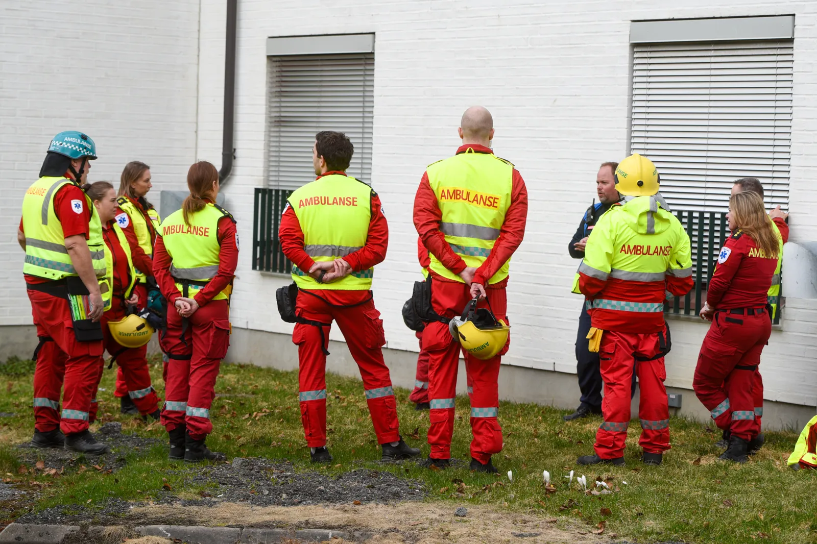 En gruppe mennesker i oransje vester står utenfor en bygning