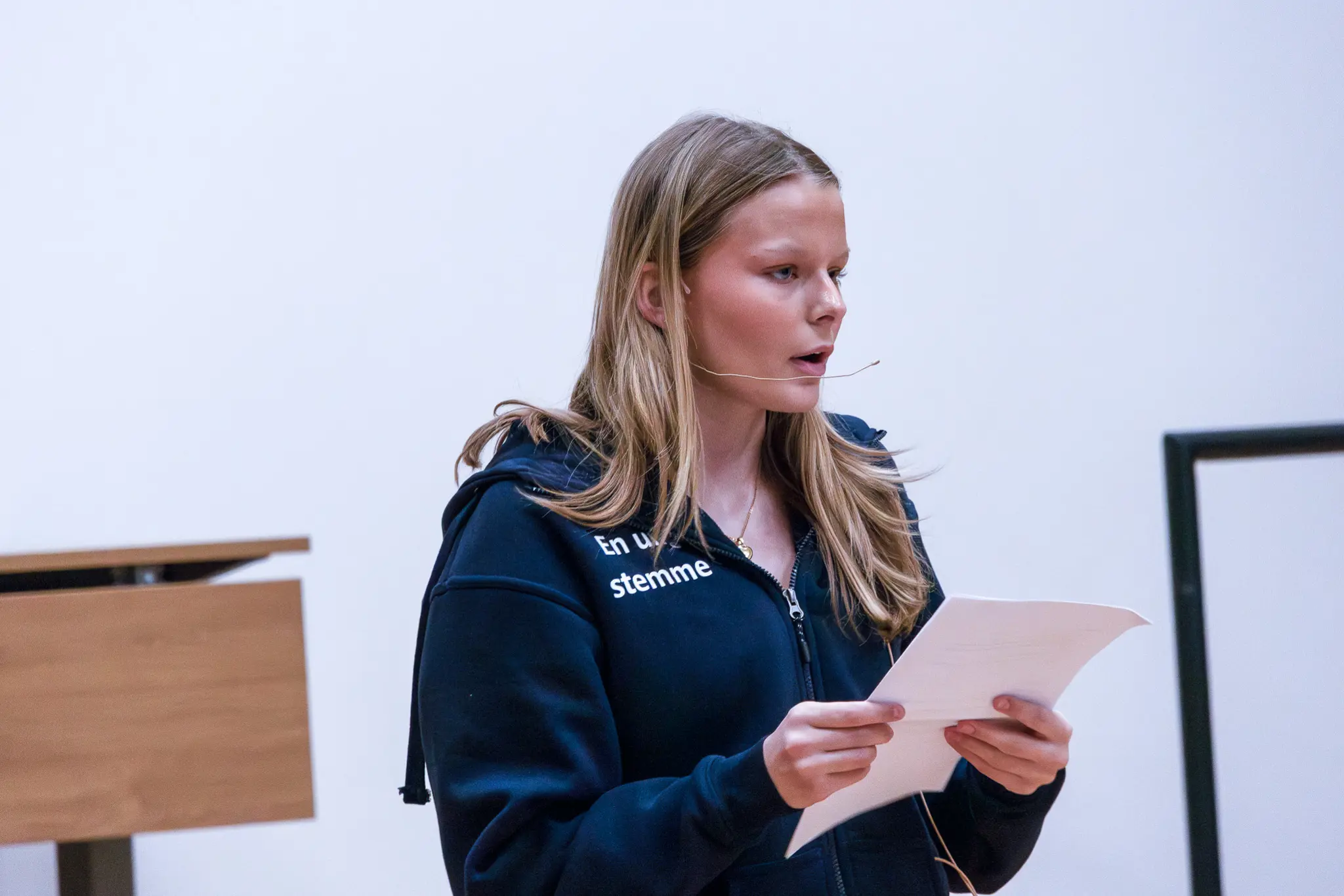 Person med hodebøylemikrofon leser fra et ark under en presentasjon i et foredragsrom.