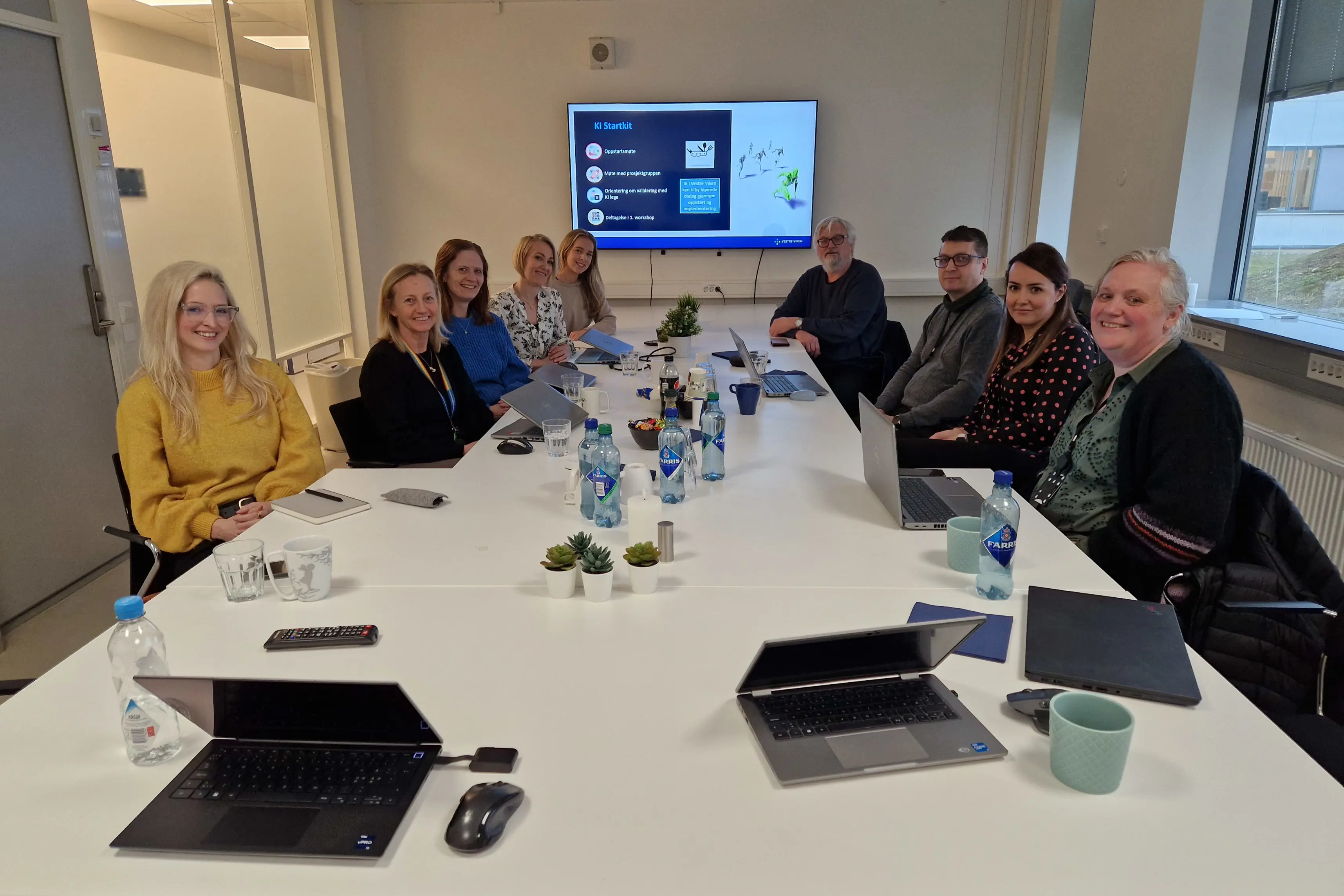En gruppe mennesker som sitter rundt et bord med en projektorskjerm