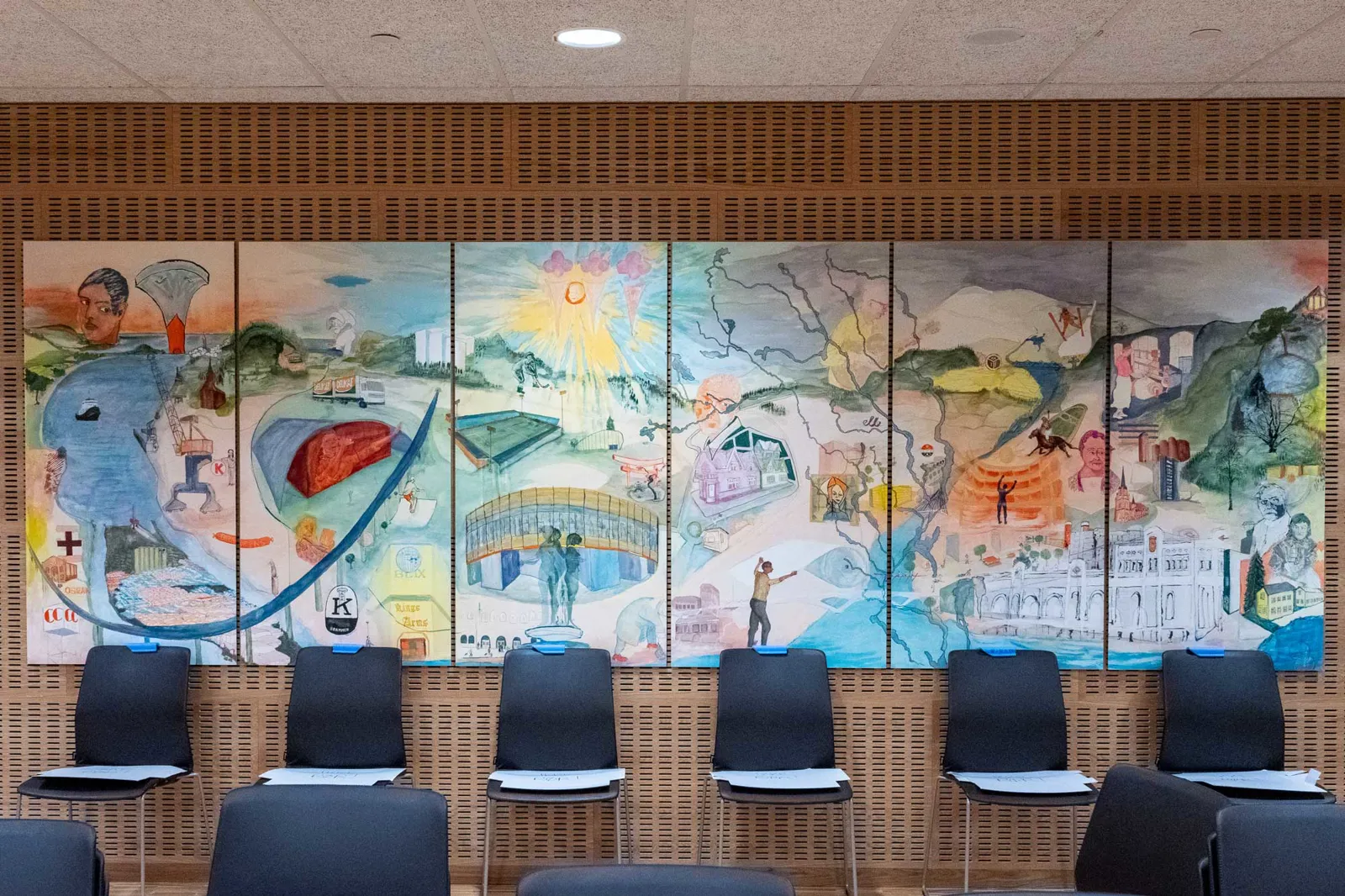 A room with chairs and a wall with art on it