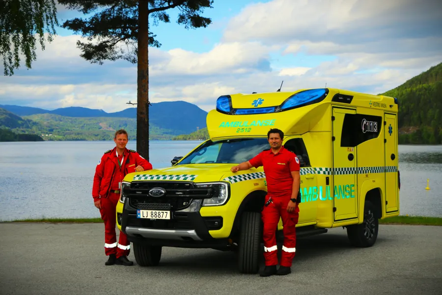 To menn står ved siden av en gul bil med blå og rød stripe