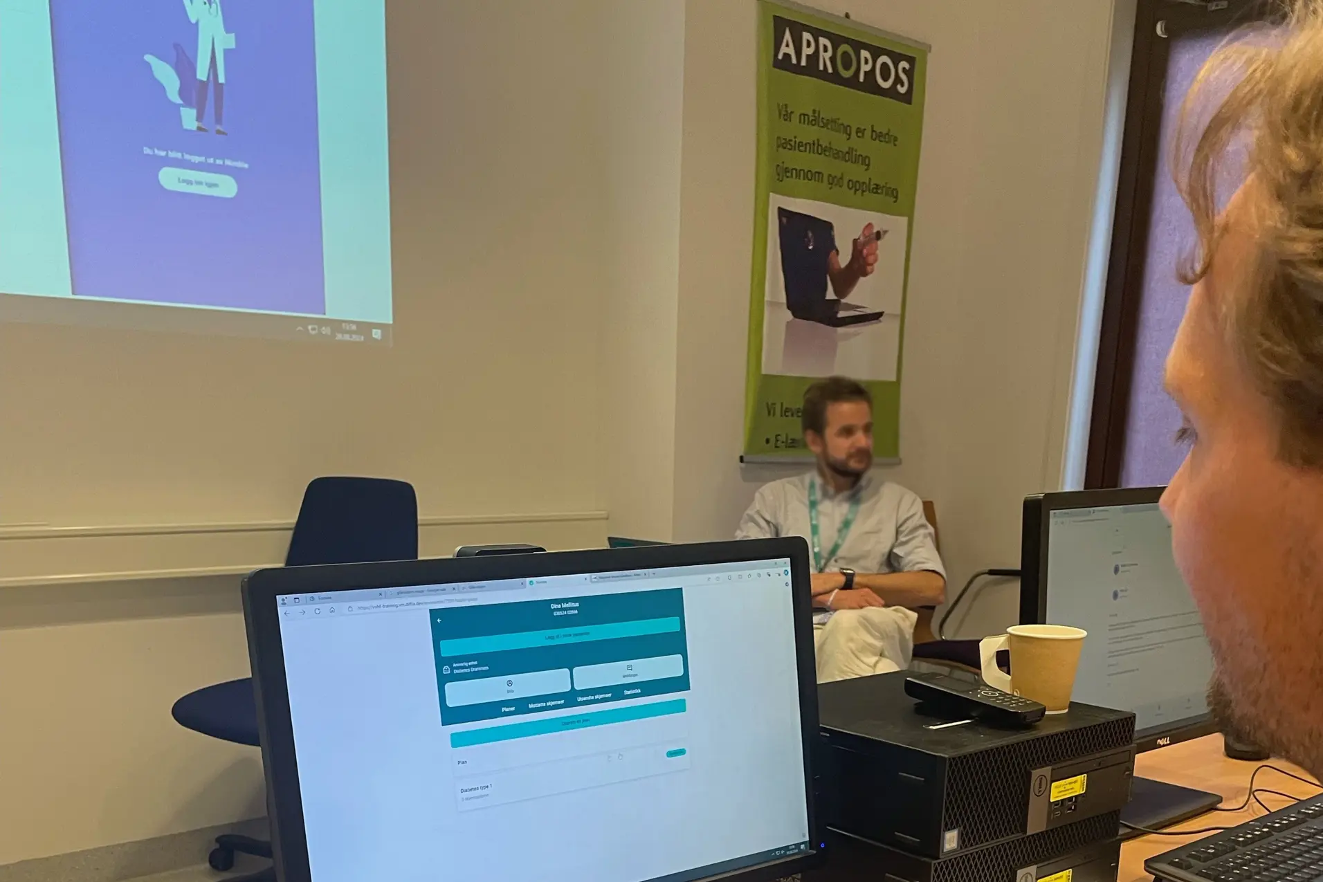 En person som sitter ved et skrivebord med en datamaskin og en person som sitter ved et skrivebord