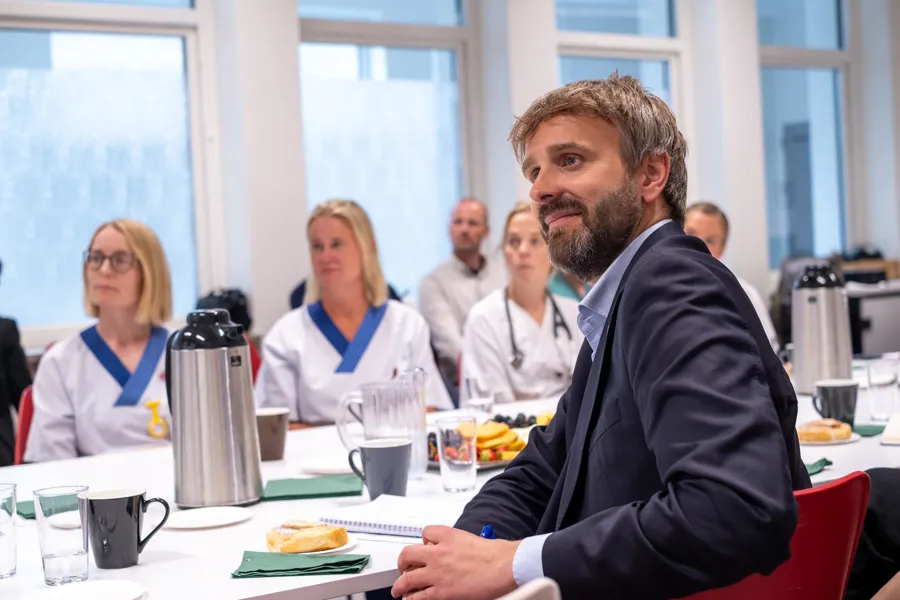 En mann som sitter ved et bord med folk i bakgrunnen