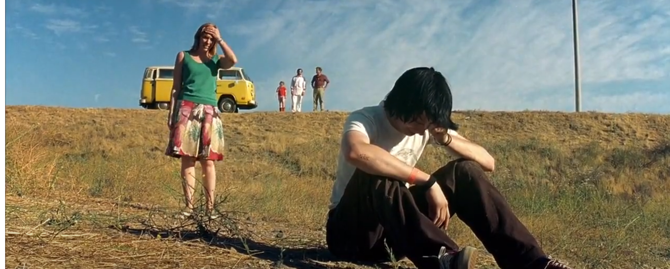 Bilde fra filmen, en ung gutt med cap sitter i veikanten og ser trist ut, mor står bak og ser fortvilet ut. 