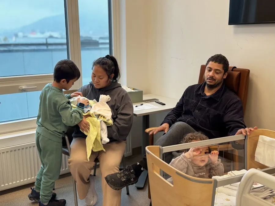 En mann og kvinne som sitter i en stol med en baby i en barnevogn med en baby i