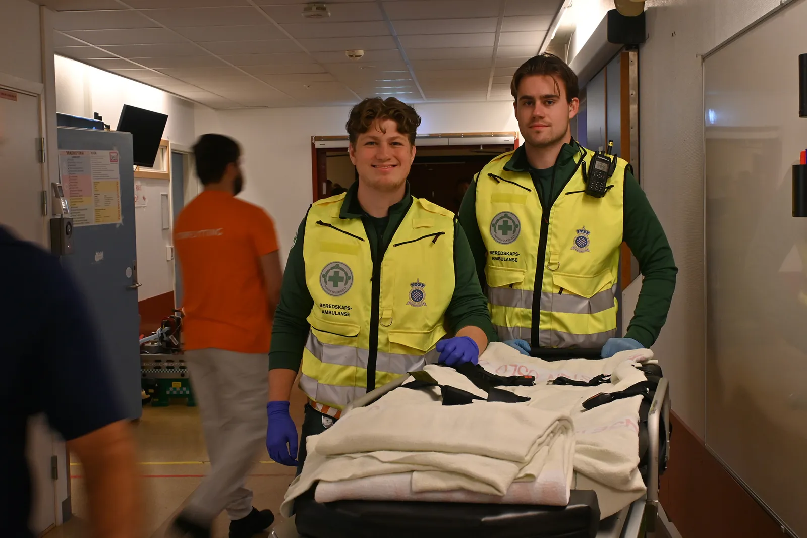 Et par menn i sikkerhetsvester som står ved siden av en seng