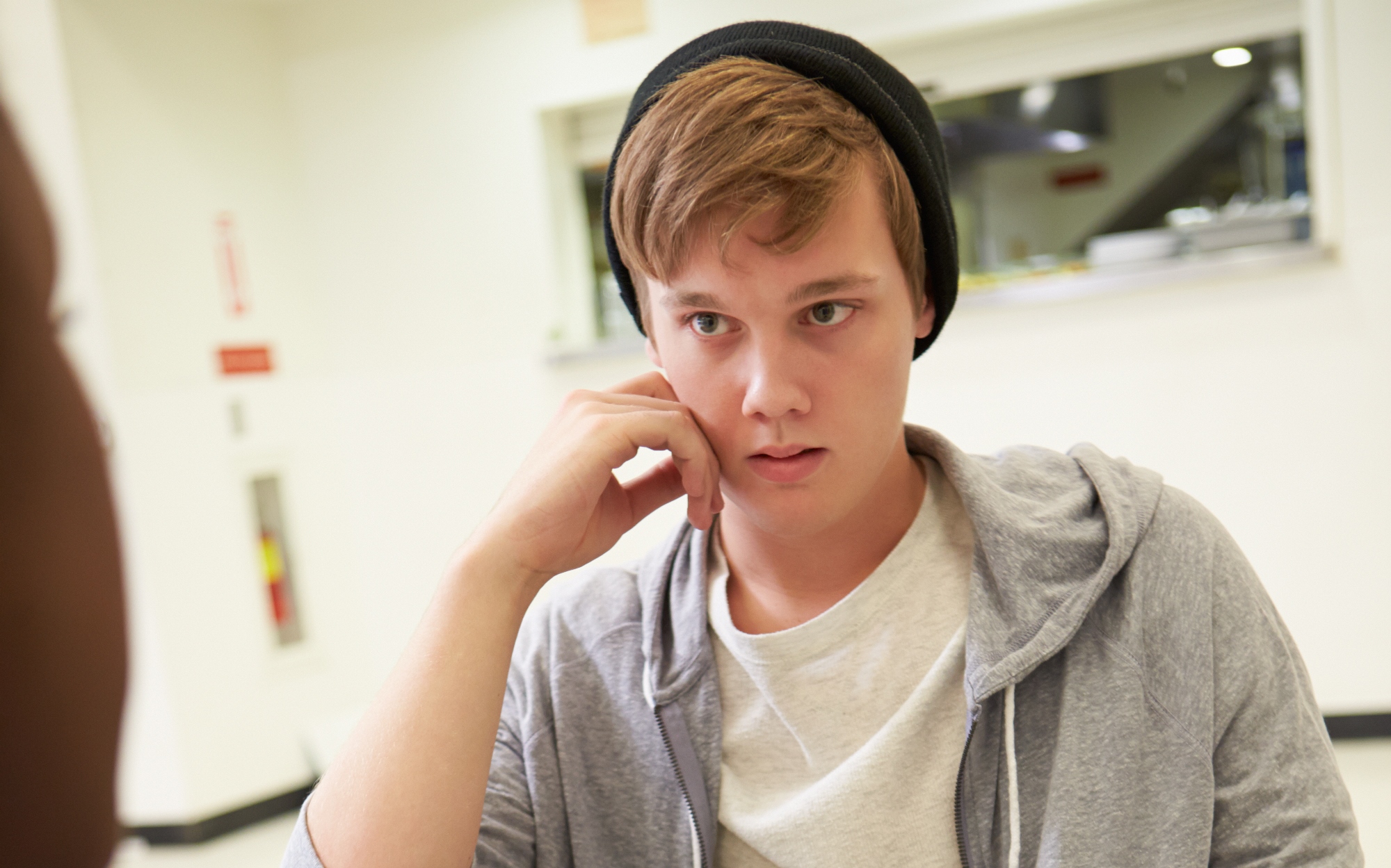 Ung elev med cap snakker med en voksen man ser bakhodet til