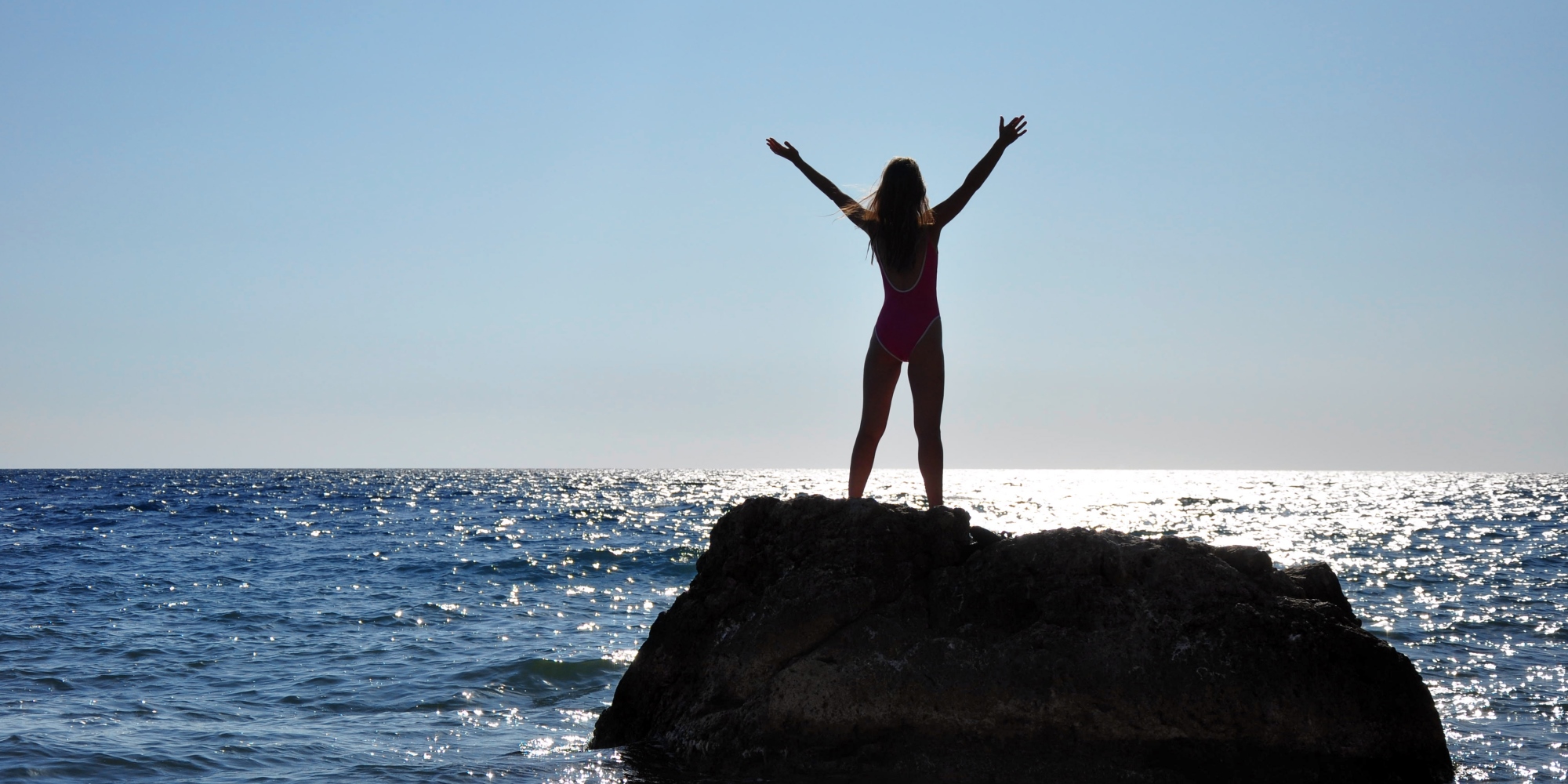 Kvinne som står på en holme og strekker seg mot himmelen.