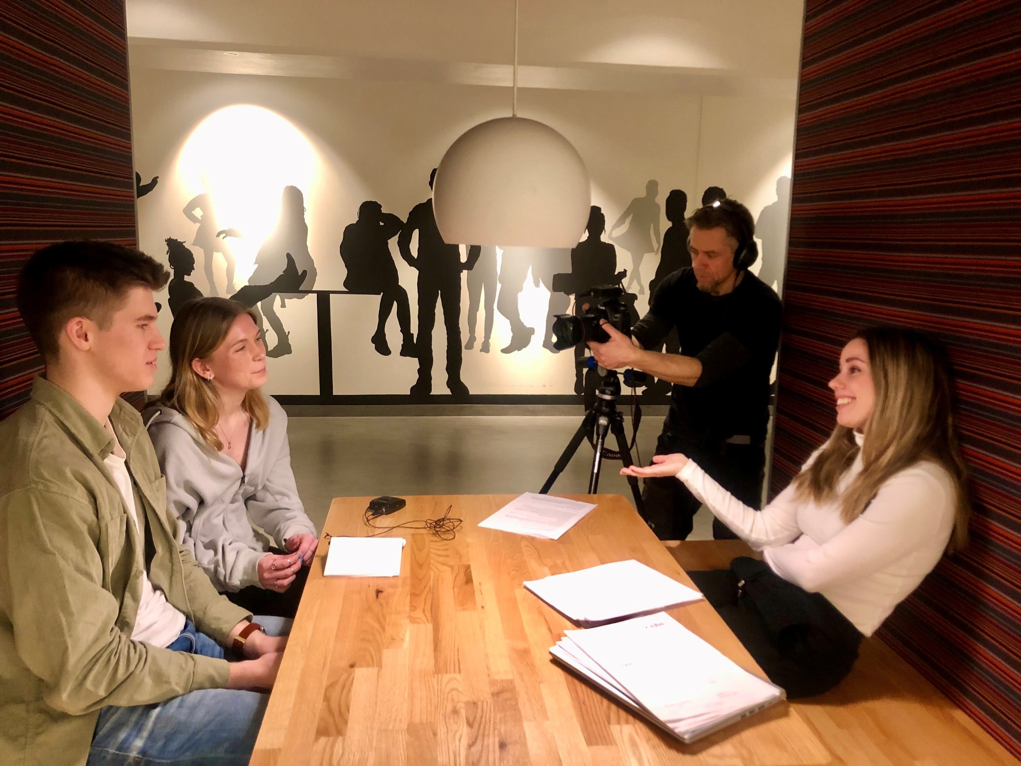 En gruppe mennesker som sitter rundt et bord med en person som står i bakgrunnen