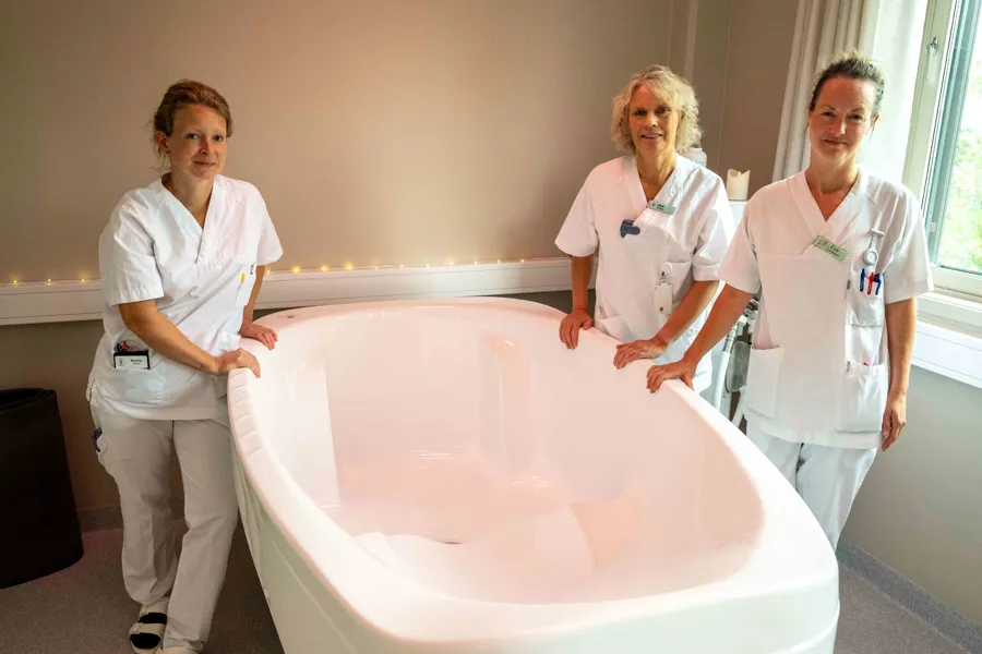 En gruppe kvinner i hvite skjorter står ved siden av et stort hvitt badekar