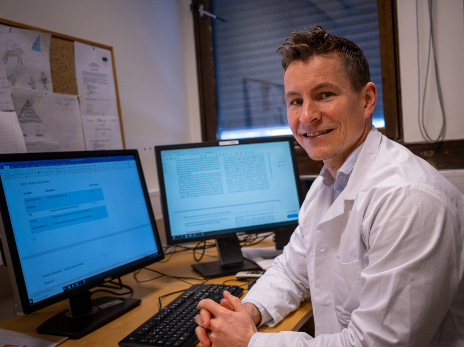 En mann som sitter ved et skrivebord med en datamaskin og en skjerm