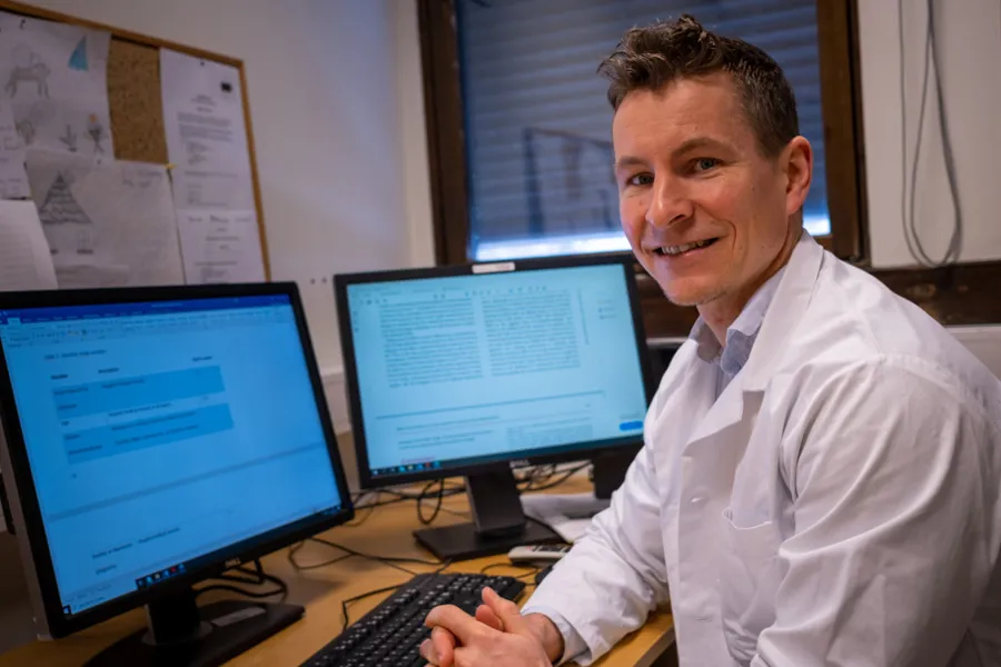 En mann som sitter ved et skrivebord med en datamaskin og en skjerm