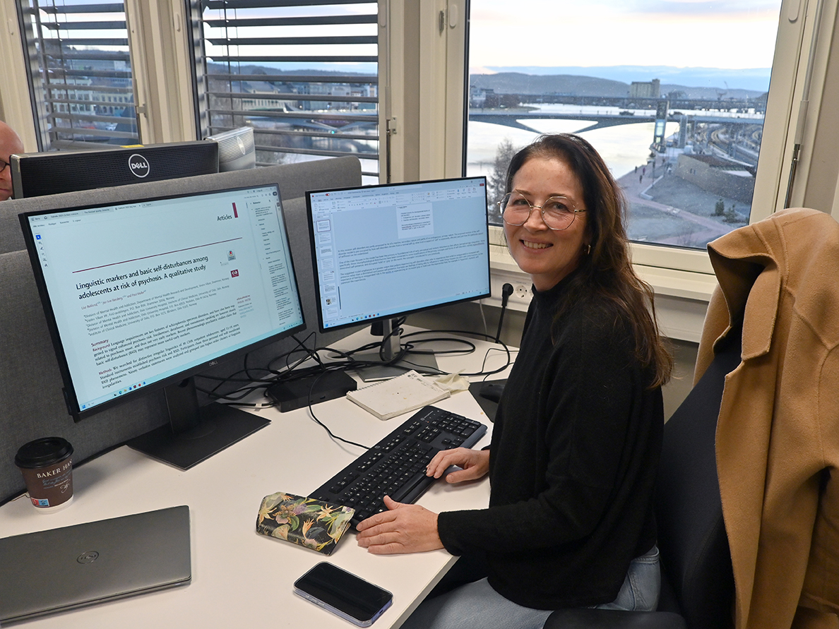 En person som sitter ved et skrivebord med en datamaskin og et vindu