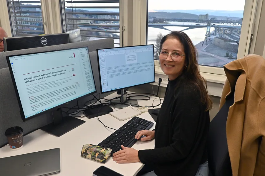 En person som sitter ved et skrivebord med en datamaskin og et vindu