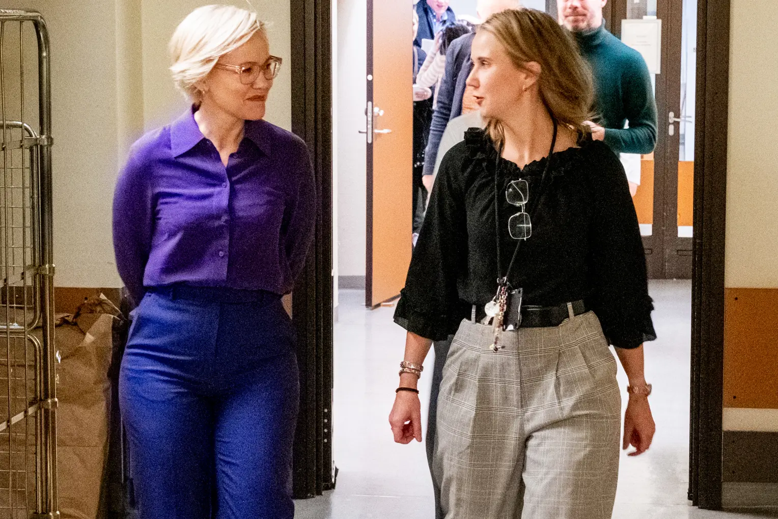 To kvinner i en ivrig samtale kommer gående ned en korridor