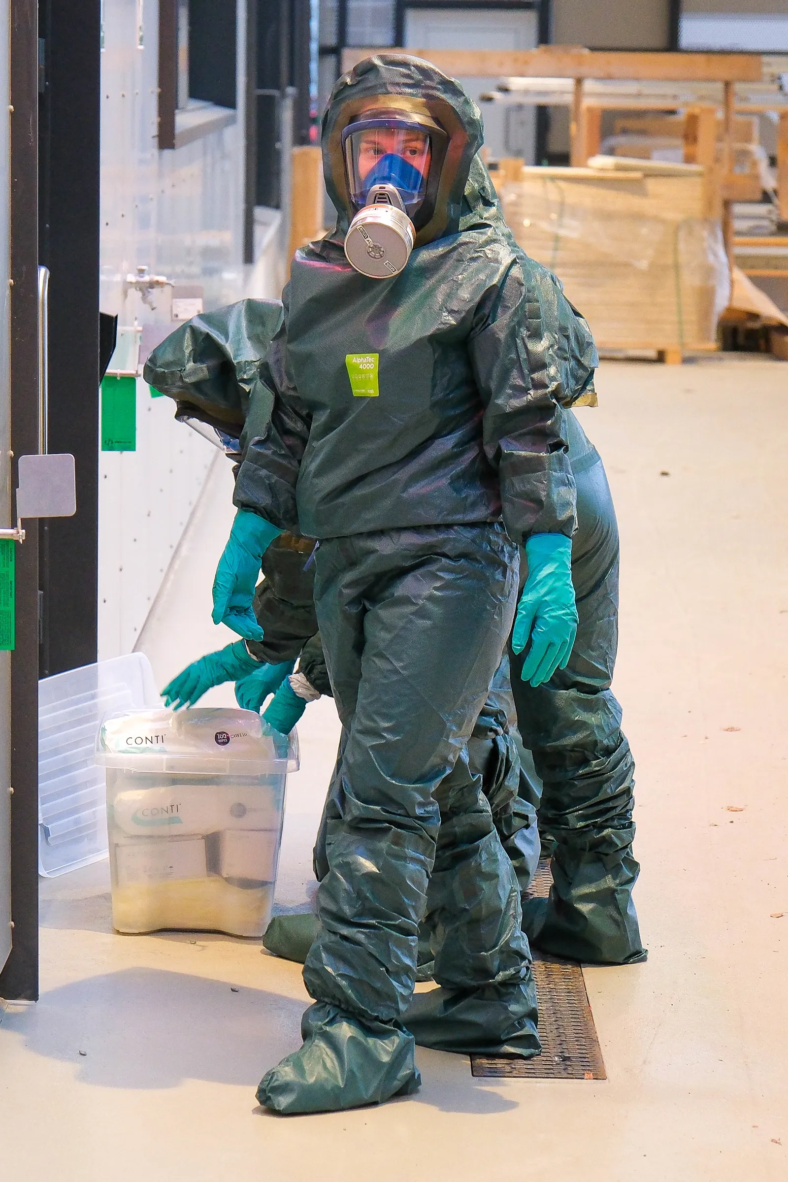 Personer i vernedrakt bærer plastkasser med utstyr.