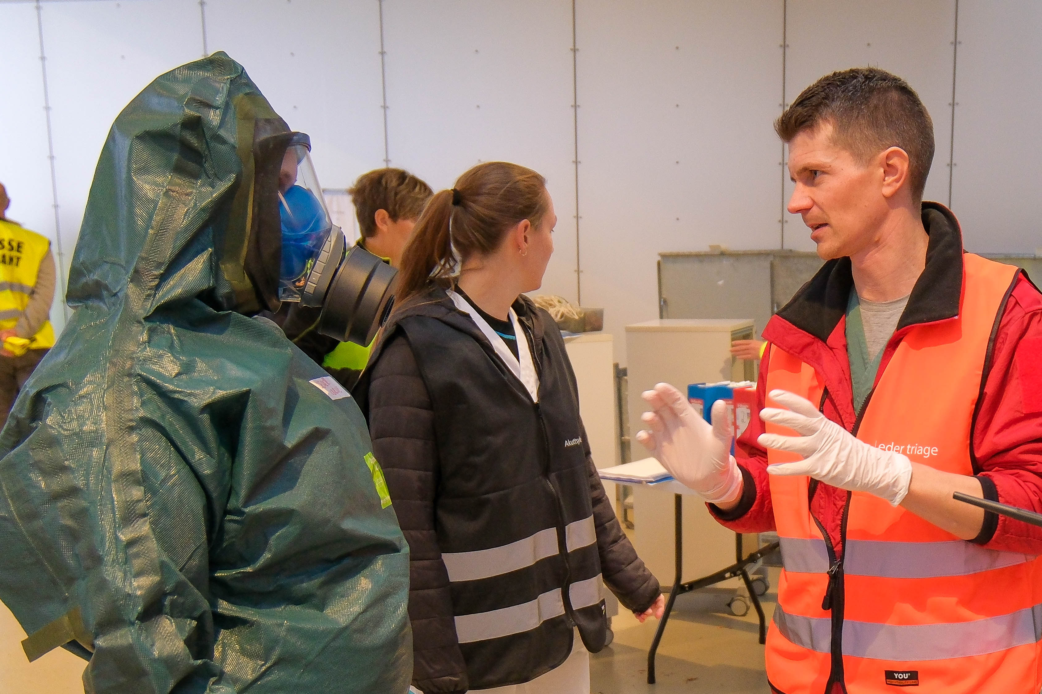 Person i vernedrakt snakker med person i rød vest som gestikulerer under øvelse.