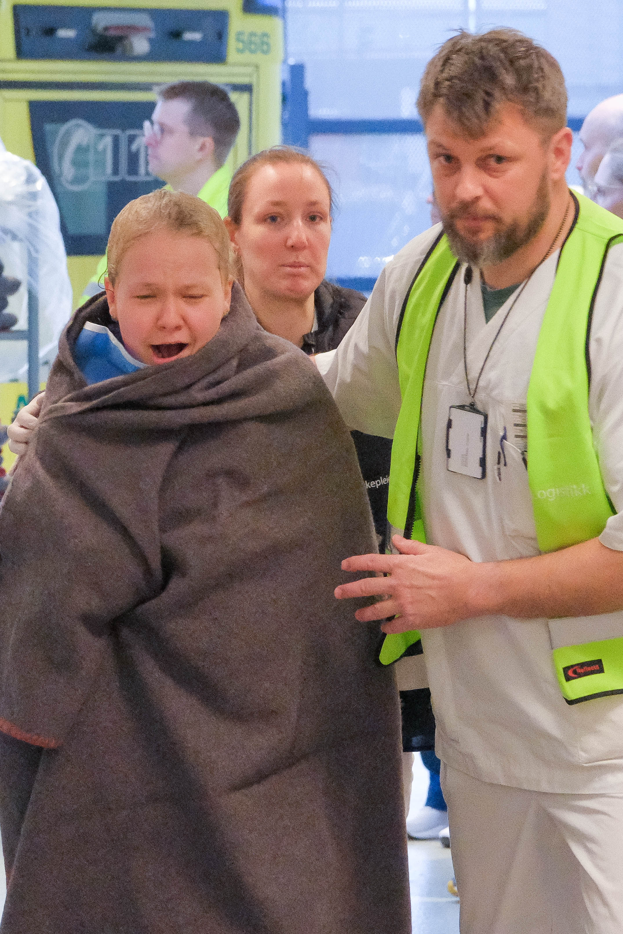 Helsepersonell med gul vest støtter person innpakket i teppe foran ambulanse.