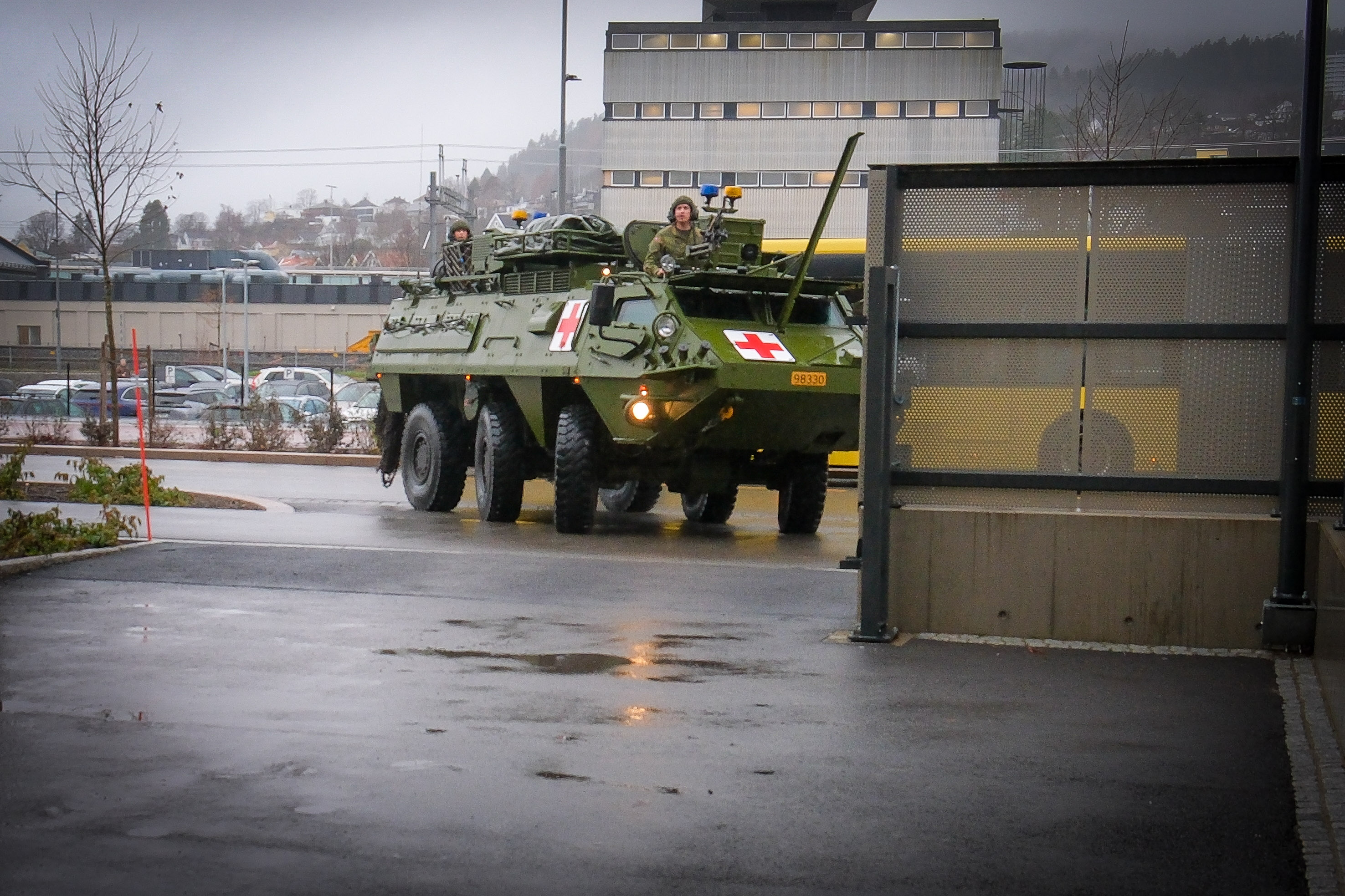 Militært kjøretøy med rødt kors kjører inn på sykehusområde med bygninger i bakgrunnen..