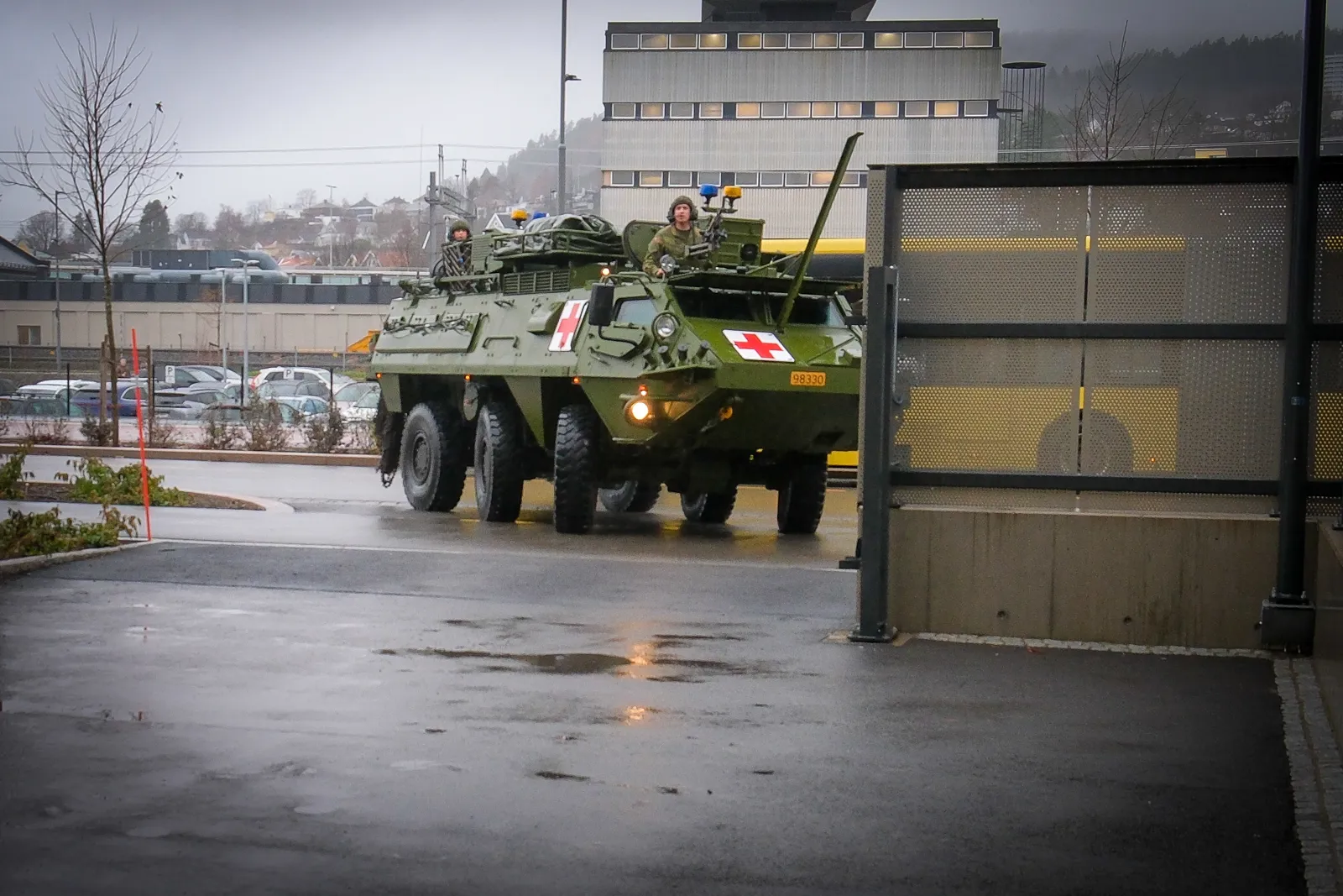 Militært kjøretøy med rødt kors kjører inn på sykehusområde med bygninger i bakgrunnen..