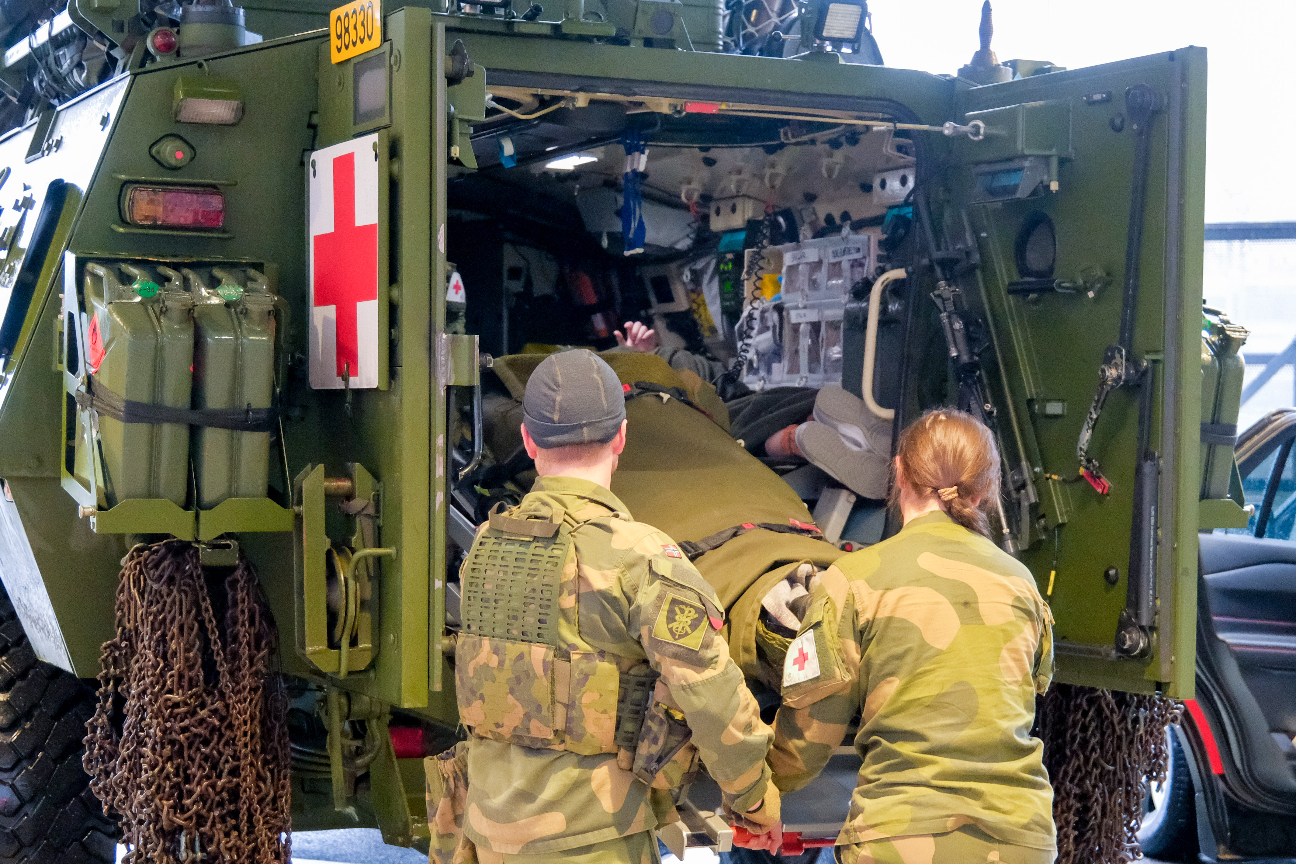 To militærpersoner løfter båre ut av grønt militært kjøretøy.