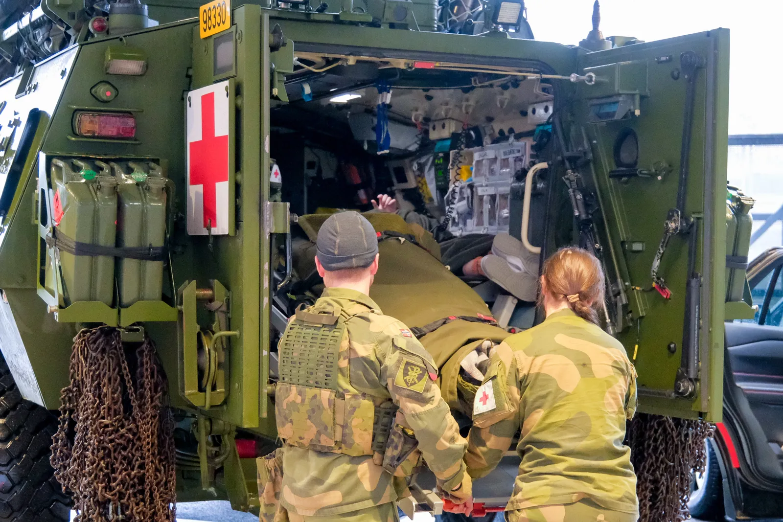 To militærpersoner løfter båre ut av grønt militært kjøretøy.
