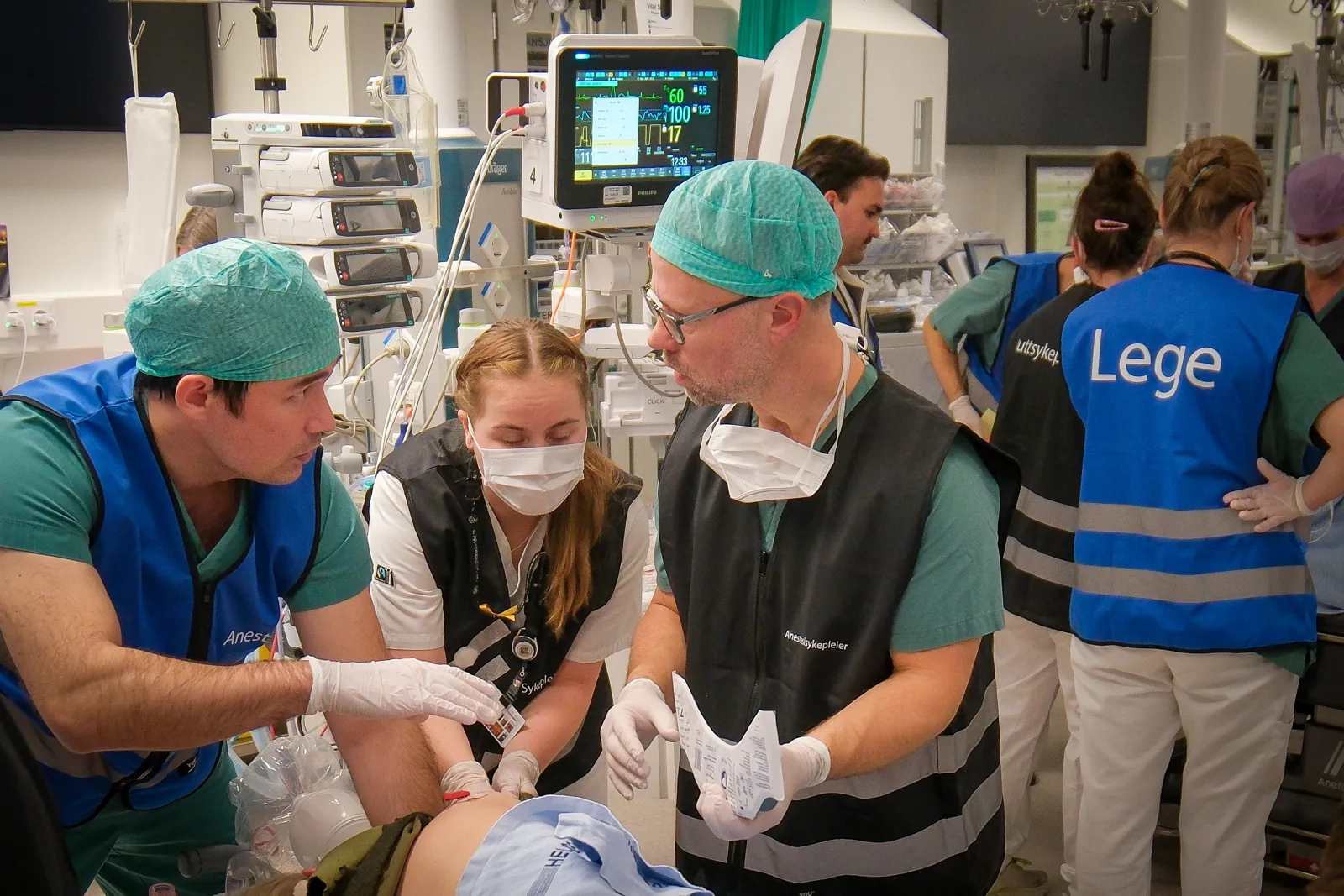 Medisinsk team behandler pasient på båre i akuttmottak med overvåkingsskjerm.