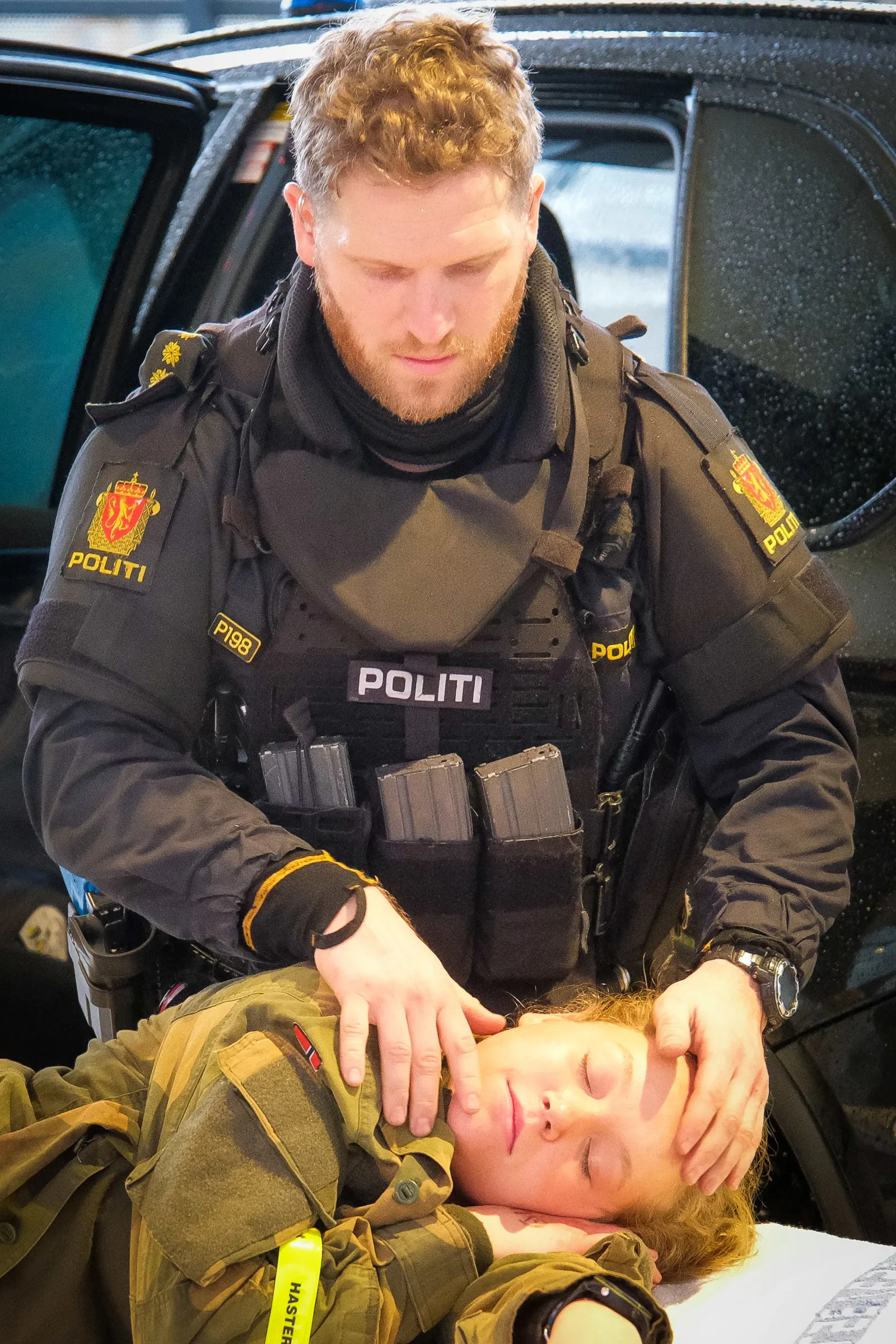 Politi holder hodet til person i militæruniform ved bil under øvelse.