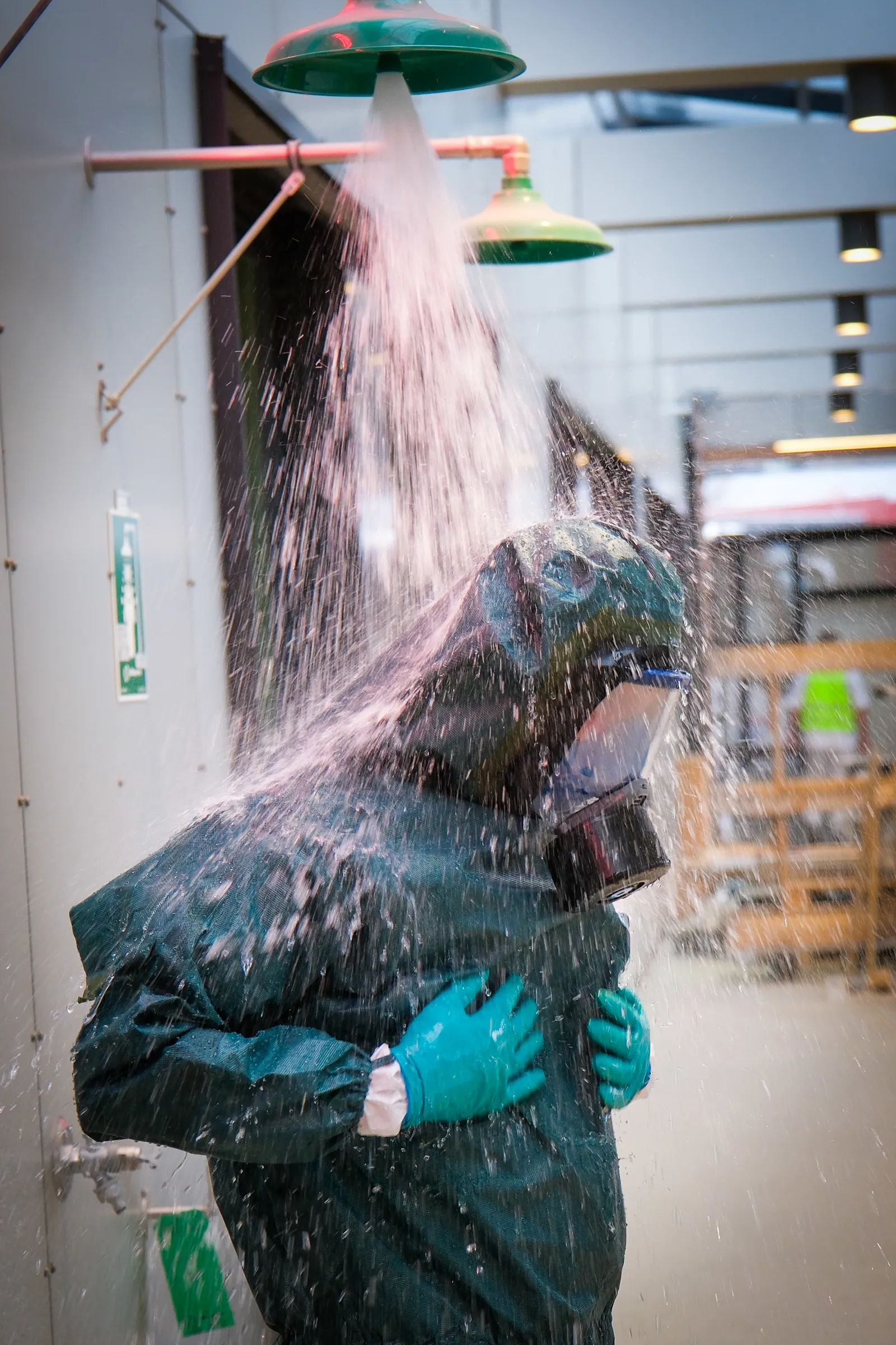 Person i vernedrakt står under dusj med vann som renner ned i en hall.