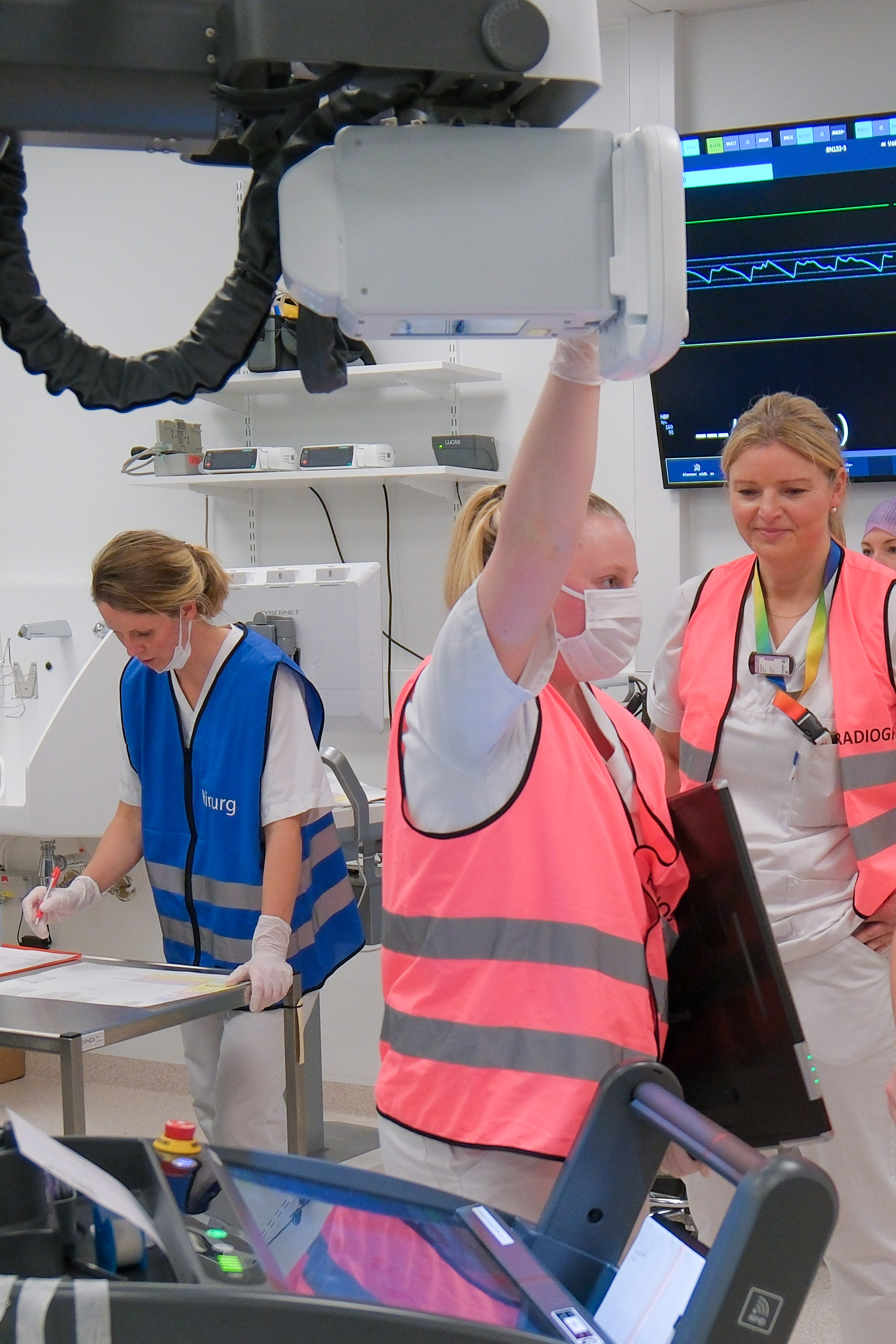 Person i rosa vest holder røntgenapparat i akuttmottak, andre jobber i bakgrunnen.