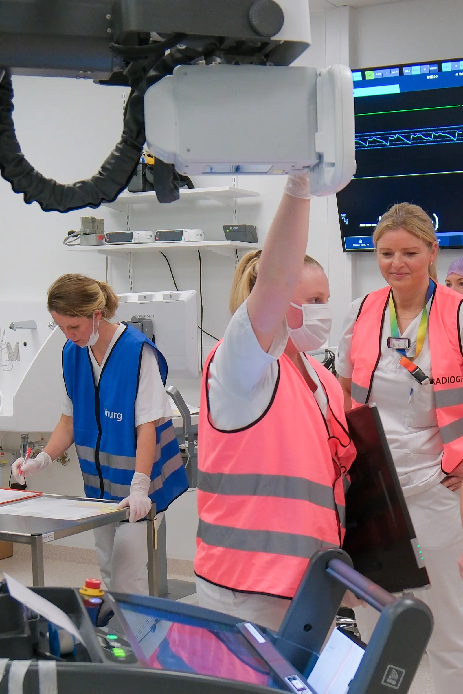 Person i rosa vest holder røntgenapparat i akuttmottak, andre jobber i bakgrunnen.