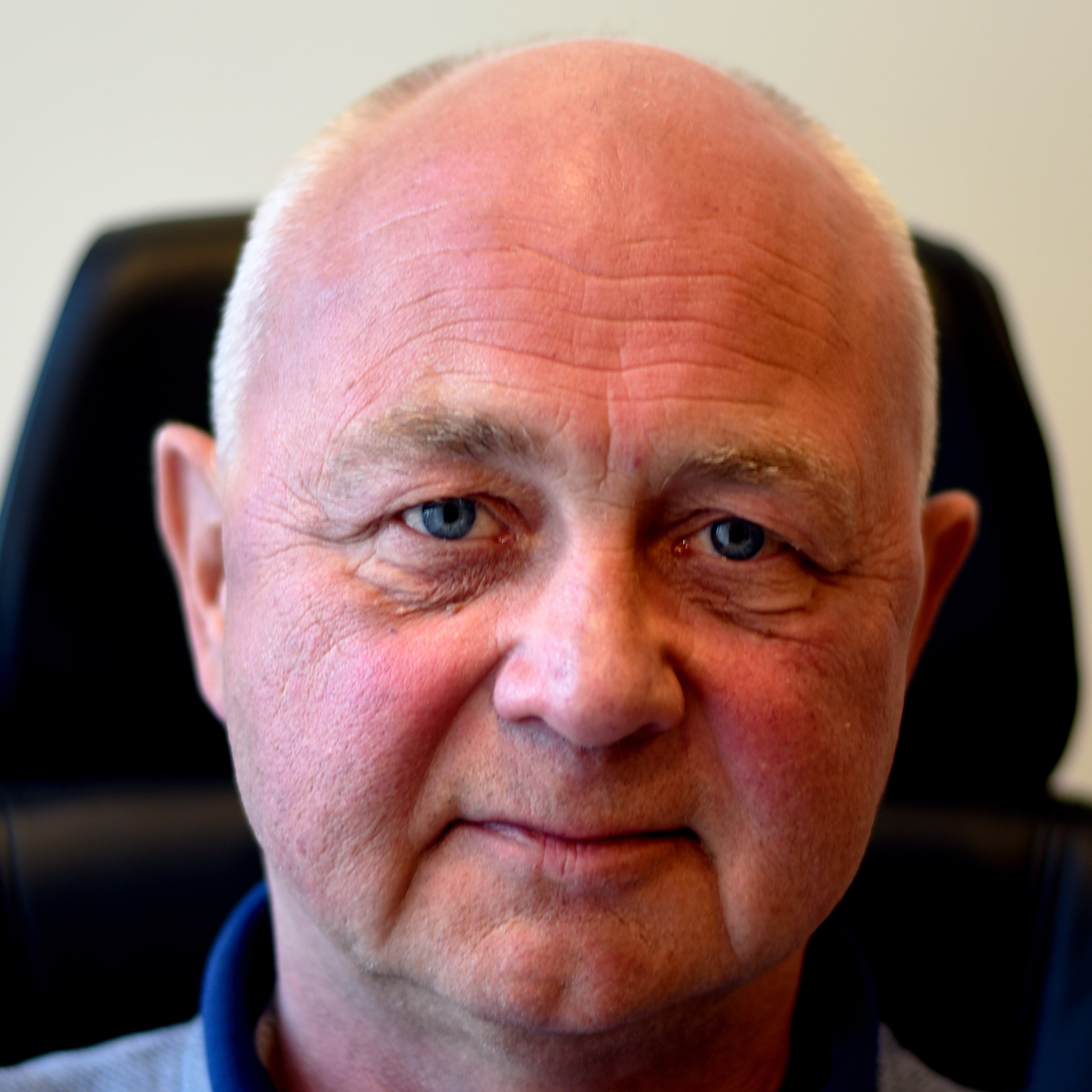 Rune Kløvtveit, with short, gray hair, wearing a blue polo shirt, sits in front of a dark chair with a light background.