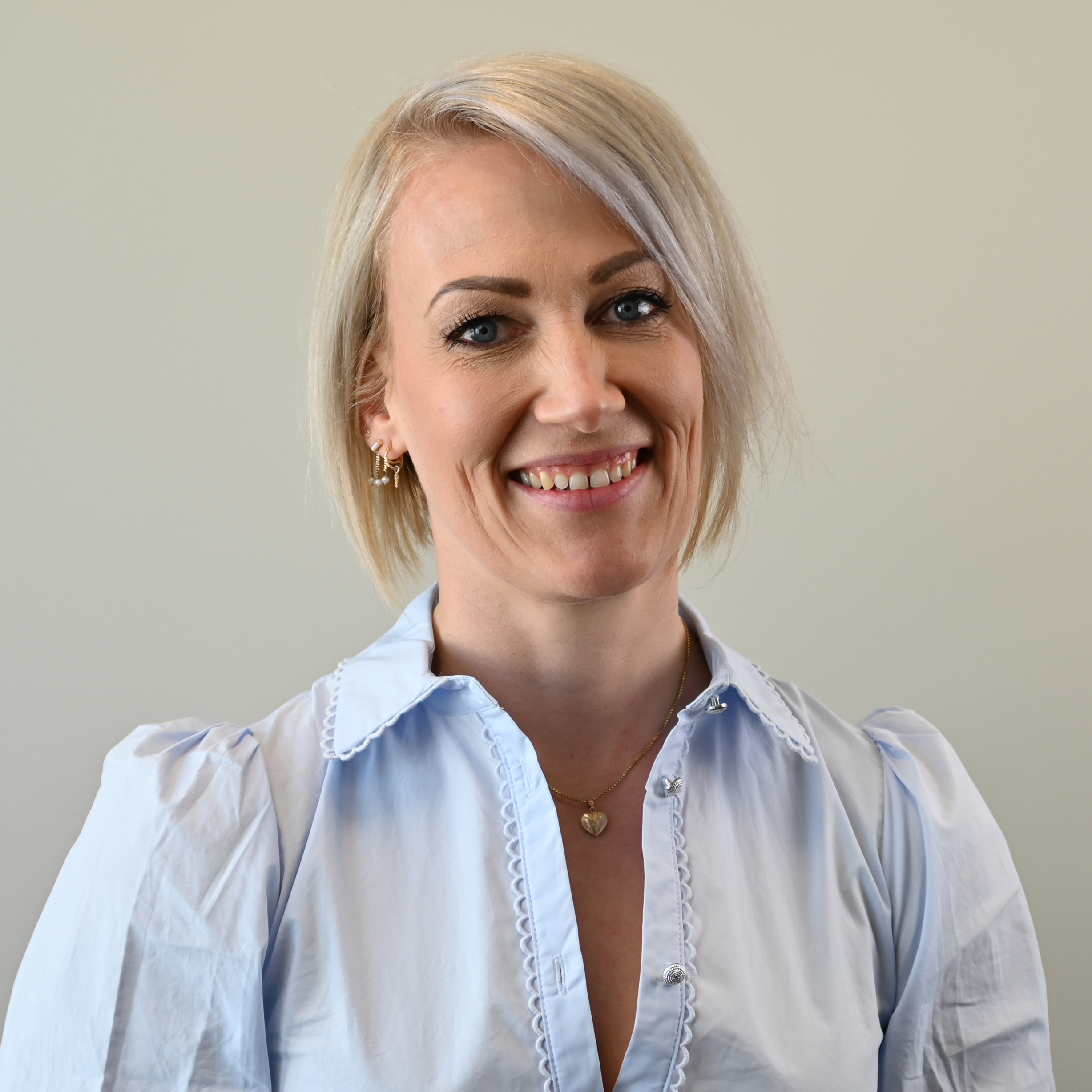 Line Tveiten, med kort, lyst hår i en glatt bobfrisyre, står innendørs foran en nøytral bakgrunn